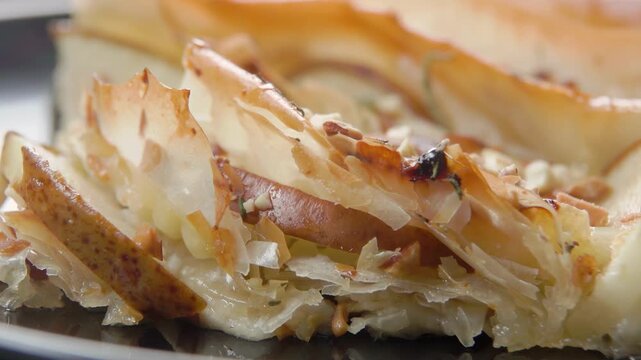 A close-up panoramic view of a slice of pie made with phyllo dough, pears, and various cheeses.