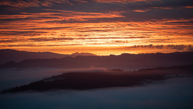 View of a tranquil landscape with layers of mountains shrouded in mist beneath a fiery sunset sky, showcasing nature's artistry, Salmon Creek, California, United States.