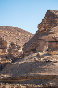 View of sun-drenched, jagged, rocky cliffs casting shadows on the sandy ground under a clear blue sky, Wadi Degla Protectorate, Cairo, Egypt.
