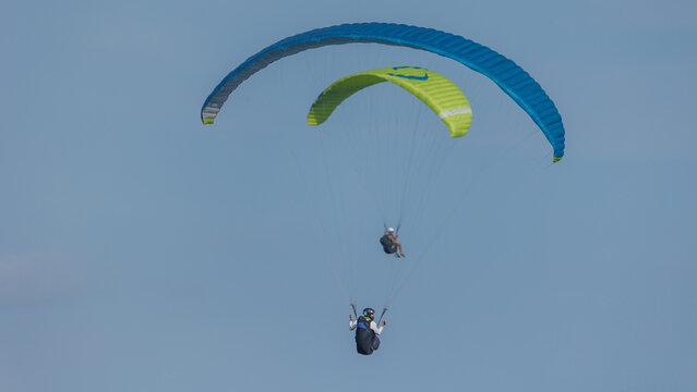 View of paragliders dance across the vast, clear sky, their vibrant canopies painting a striking contrast against the serene blue canvas, Wilderness, Western Cape, South Africa.