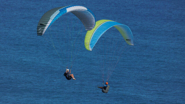 View of paragliders soaring in the sky above the vast, blue ocean waters, with their colorful canopies contrasting the deep blue of the sea, Wilderness, Western Cape, South Africa.