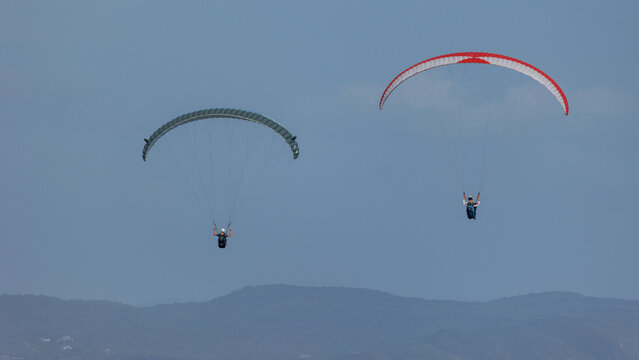 View of two paragliders soaring high above the distant mountains against a clear sky, a vibrant display of adventure, Wilderness, Western Cape, South Africa.