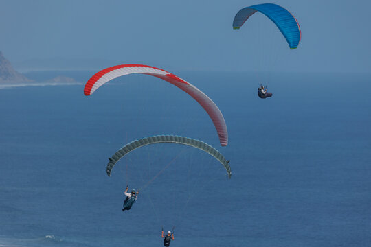 View of paragliders dance in the sky above the ocean, their colorful canopies contrasting with the deep blue sea, creating a thrilling spectacle, Wilderness, Western Cape, South Africa.
