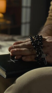 Vertical close-up shot of hands of unknown catholic man with prayer beads closing leather-covered holy bible and reflecting on gods plan