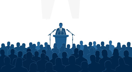 A speaker stands at a podium addressing a large, attentive audience in a dimly lit room with spotlights overhead. © Candrani