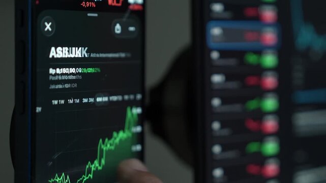 close up smartphone with laptop and open stock exchange, trading Online app interface. Man hand scrolling touch screen analysing chart forex crypto currency.