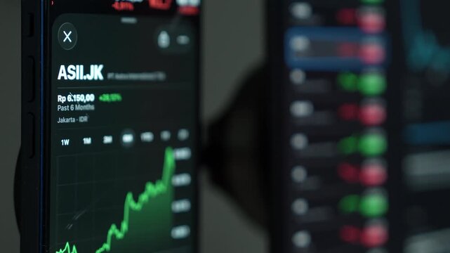 close up smartphone with laptop and open stock exchange, trading Online app interface. Man hand scrolling touch screen analysing chart forex crypto currency.