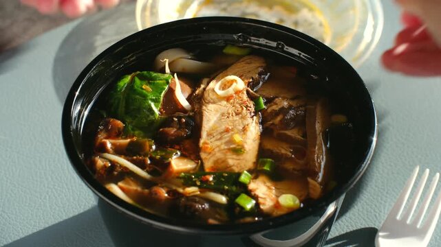 Hands open plastic lid from hot takeout container asian noodle soup ramen with chicken and vegetables, ready to eat for delicious, convenient lunch on sunny day. Hands open takeout container of ramen
