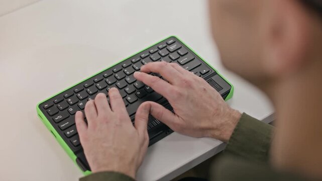 High angle cropped shot of hands of unrecognizable blind person using computer keyboard with braille display while sitting at desk indoors