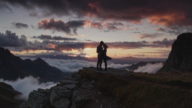 A man and woman looking at a mountain sunset, then embracing, and finally standing closer on a rocky peak over clouds at dusk