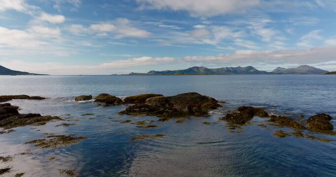 Aerial low dolly of rocky coastline and calm sea of Aarnessan Stokmarknes in northern Norway, establishing backdrop