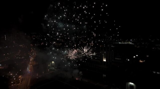 Drone view of fireworks blooming over Brussels city lights, with smoke trails and sparkling bursts above the skyline during a New Year festival night.