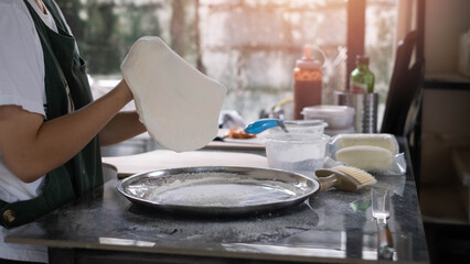 Close-up of pizza dough being stretched by hand in kitchen, homemade baking process, fresh ingredients and preparation tools, artisan food, authentic cooking lifestyle, traditional pizza making.