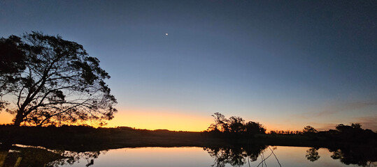 Twilight landscape with calm lake reflection and crescent moon