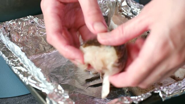 Female hands carefully arranging fresh, seasoned pieces raw pollock fish on baking tray lined with shiny aluminum foil, preparing seafood for baking or grilling in kitchen