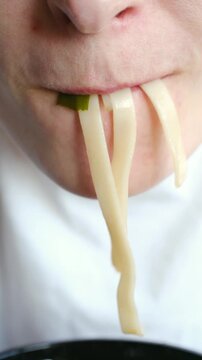 Extreme close up shot capturing person mouth while slurping thick, white udon noodles from bowl, highlighting enjoyment of traditional japanese meal and authentic eating. Person slurping udon noodles