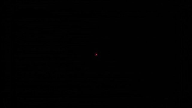 A small red light appears in a completely black background with a deep and mysterious atmosphere.