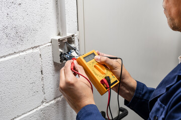 Close-up on an hands of electrician fixing an electrical outlet and measuring the voltage at a factory - improvement concepts
