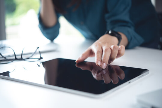 Close up, business woman using digital tablet with laptop computer on office table. Woman finger touching on tablet screen, searching the information, internet networking at workplace