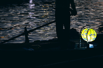 Silhouette of person rowing boat with glowing lantern on water at night © VERSUSstudio