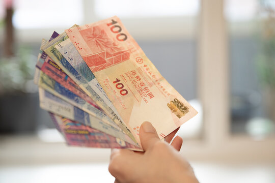 Woman holding a fan of Hong Kong dollars banknotes. Concept of finance, wealth, currency exchange, budget, and business investment.