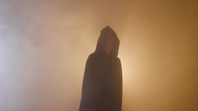 A mysterious man in a black hooded cloak performs dramatic gestures against a bright, warm light shining from behind him, evoking a secret order of mages and mystics.