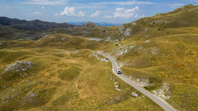 Aerial view of a camper van driving along a winding road at Sedlo Pass in Durmitor, Montenegro, surrounded by rugged mountain landscapes, capturing freedom, adventure, and scenic road travel.