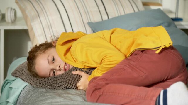 Tired preteen boy child lying down on bed with pillows resting during day while watching TV in bedroom, AI generated footage