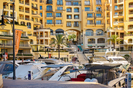 St. Julian's, Malta - November 3, 2025: View of a modern waterfront promenade with a luxury residential complex with restaurants, moored yachts, palm trees, and Portomaso flag.