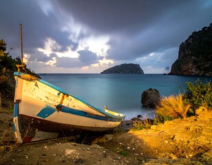 Abandoned boat sits on a sandy shore, with hills and a rocky island in the distance under a cloudy sky