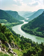 A winding river flows through a lush, green valley surrounded by mountains under a cloudy sky