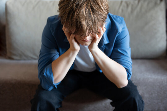 Young man (zoomer) sitting and holding his head in stress, burnout and mental exhaustion.