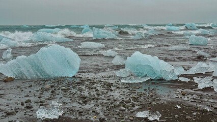Dramatic and out of this world landscape of blue icebergs and diamond like ice washed ashore in the black sands of Diamond Beach in south Iceland