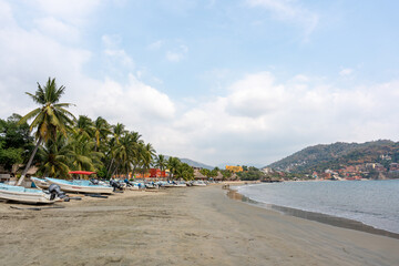 Fototapeta premium View of the beach in the bay of Ixtapa Zihuatanejo with boats in the sea and palm trees on the sand. Tropical landscape of costa grande, Guerrero. Mexico, January 19, 2026.