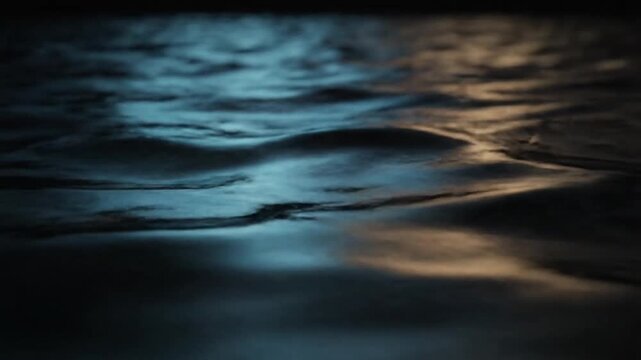 Gentle dark water ripples reflect striking turquoise and amber lights, creating an abstract, dynamic texture across the surface in this low-light environment.