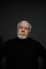 Obraz premium Elderly man with a beard poses in a dark setting while looking forward during a photo session
