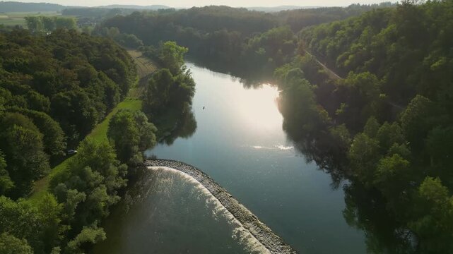 Aerial view of the Kolpa River near Metlika, Slovenia, featuring a small river dam with flowing water, calm green river pools, surrounding forest, and a peaceful rural landscape in summer.