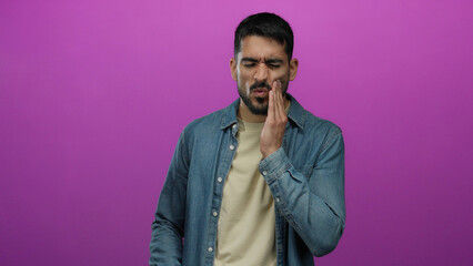Fototapeta premium Man suffering toothache against pink background looking uncomfortable and distressed while touching his cheek.