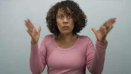 Woman with curly hair wearing a pink top raises both hands at head level against a grey studio...