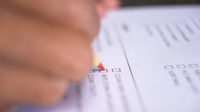 Person's hand marking a series of checkboxes on a document or form with a pencil during a task