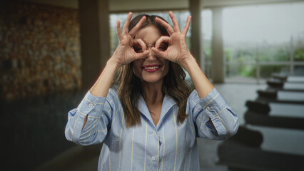 Woman wearing glasses sticks out tongue and raises bare arms in spa building pool area; carefree...