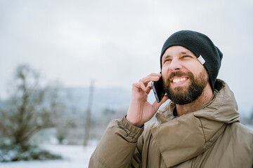 Portrait of young man in snowy park. Uses smartphone. Winter concept.