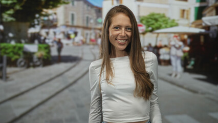 Fototapeta premium Woman pointing finger directly at camera on a cobblestone street, smiling broadly while wearing a cropped white top that reveals a small midriff; joy invitation.