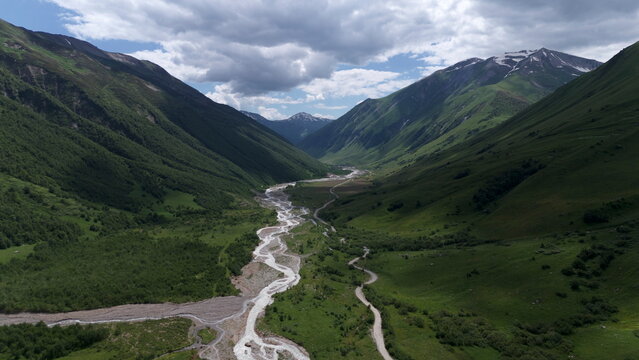 Aerial drone view of a lush mountain valley near Ushguli, one of the highest continuously inhabited villages in Europe, located in the Svaneti region of Georgia. A winding river flows through green al