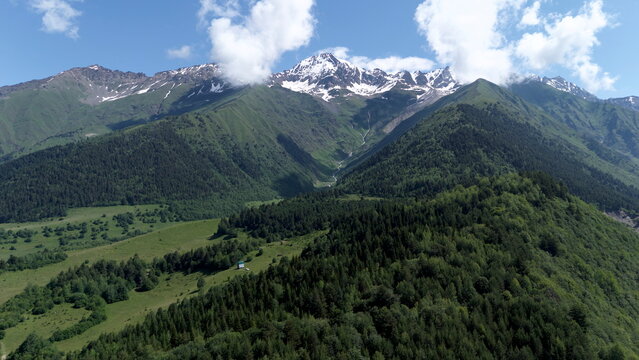 Aerial drone landscape of Mount Ushba, one of the most iconic peaks of the Caucasus Mountains, overlooking the green valleys and alpine villages near Mestia in the Svaneti region of Georgia. Snow-capp