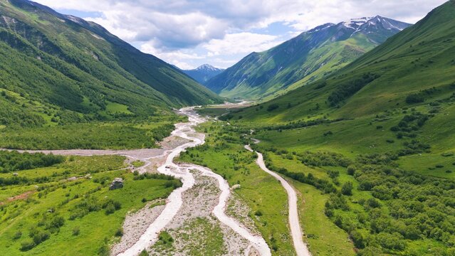 Aerial drone view of a lush mountain valley near Ushguli, one of the highest continuously inhabited villages in Europe, located in the Svaneti region of Georgia. A winding river flows through green al