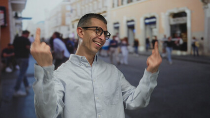 Naklejka premium Man smiling making rude gesture with both hands on busy street with blurred pedestrians and buildings in background