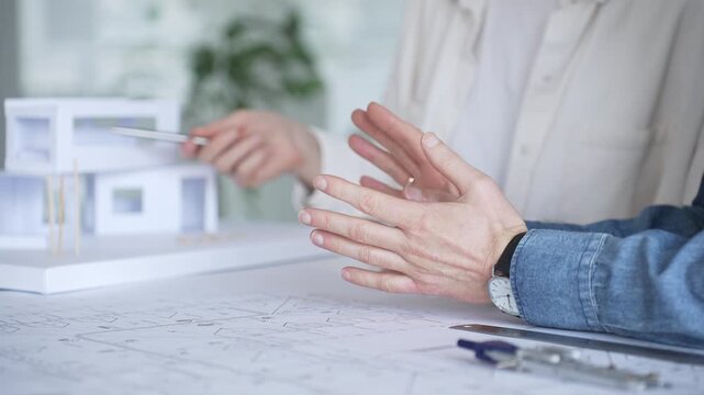 Architects collaborating on blueprint plans, discussing engineering details and project designs, planning construction development with a laptop in a modern office environment