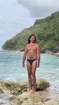 Male Freediver With Outstretched Arms On Coastal Rock, Head Tilted Toward Cloudy Sky, Chest Open To Sea Breeze, Turquoise Surf And Spray, Island Cliff Behind, Expressive Triumphant Stance, Dynamic