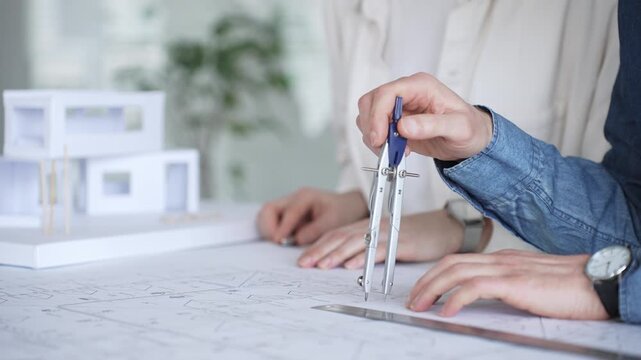 Architects collaborating on blueprint plans, discussing engineering details and project designs, planning construction development with a laptop in a modern office environment